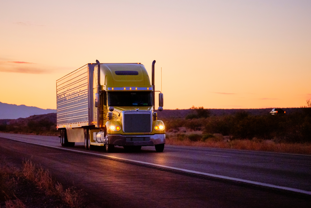 Semi-truck driving on highway with bright yellow sunset.